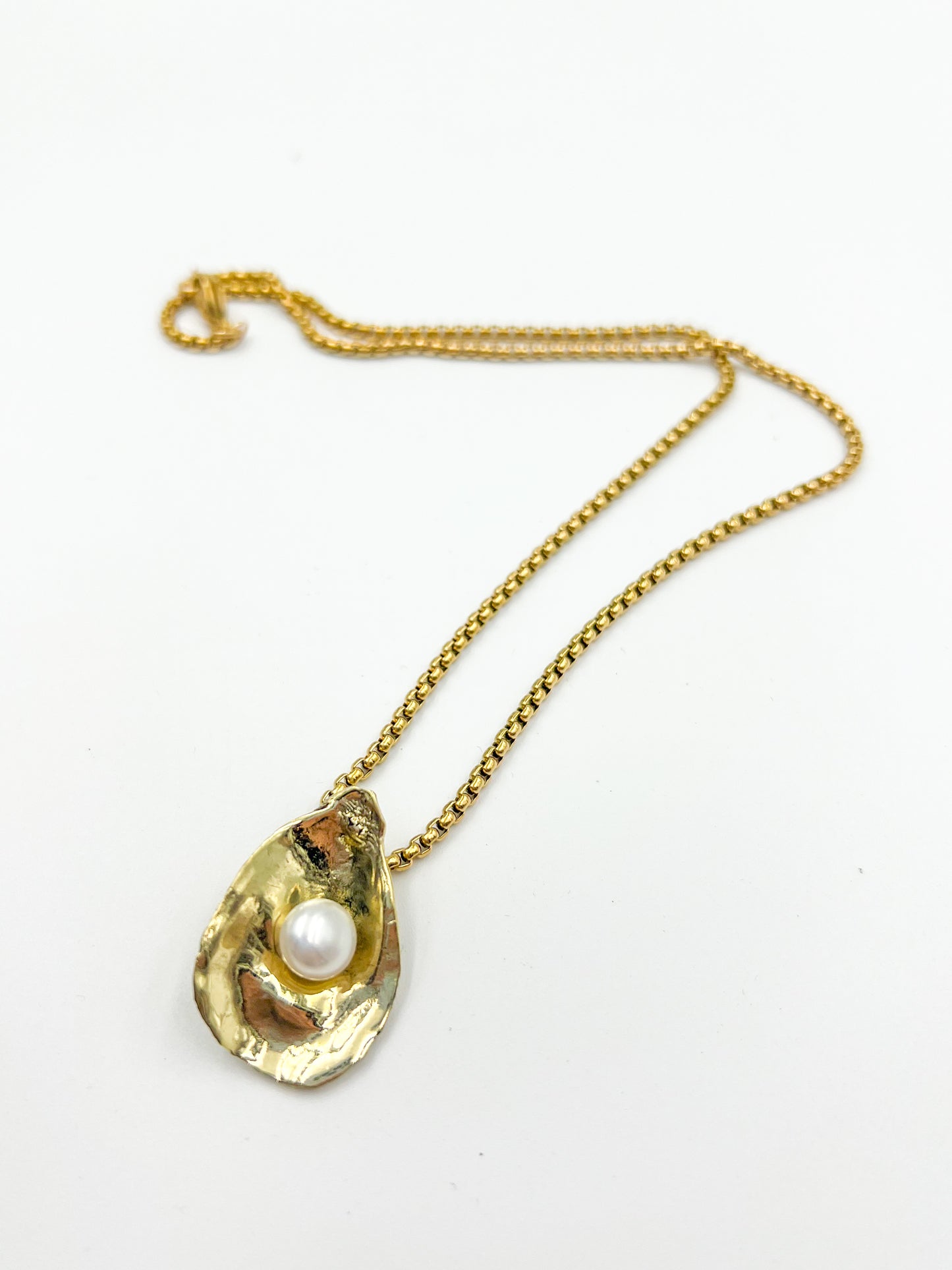 Gold necklace with an oyster shell and pearl pendant on a white background