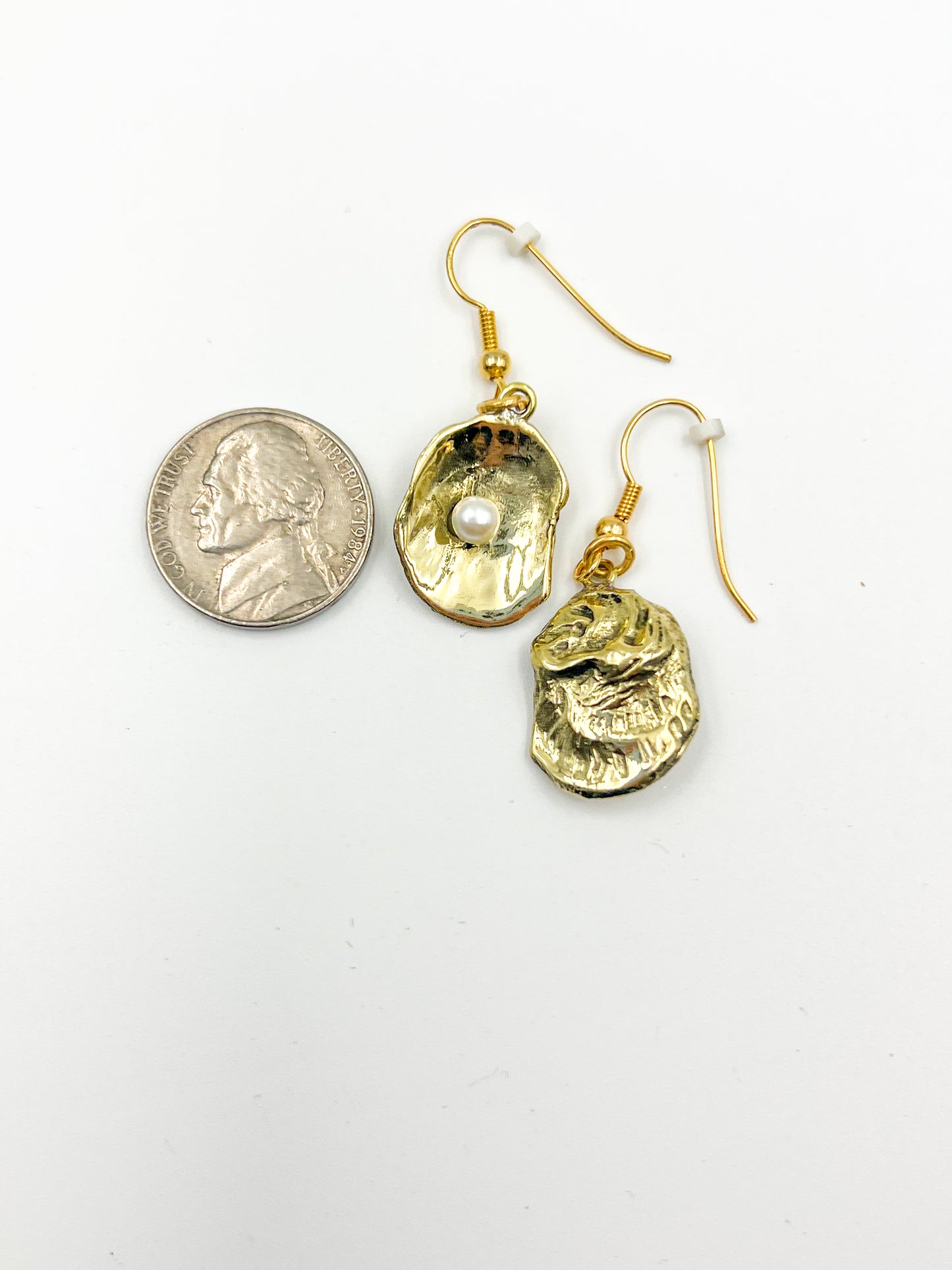 Gold earrings next to a nickle on a white background