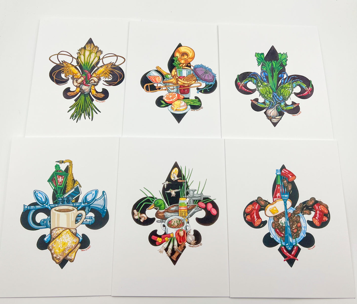 Six square art prints arranged in a 2x3 grid on a white background, each featuring a colorful fleur-de-lis motif filled with different Mardi Gras-themed illustrations such as food, masks, beads, and festive objects.