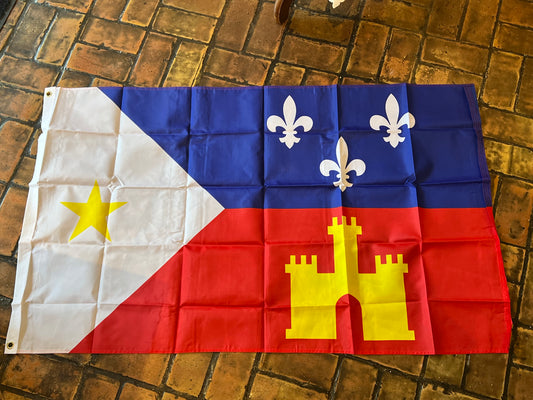 A Acadian provincial flag laid flat on a brown brick floor, showing the white triangle with a yellow star, blue upper-right field with white fleurs-de-lis, and red lower-right field with a yellow castle.