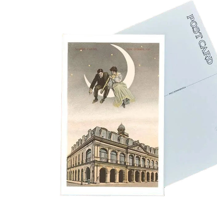 Vintage-style postcard with a couple under a crescent moon, placed on a wooden surface with an envelope and pen.