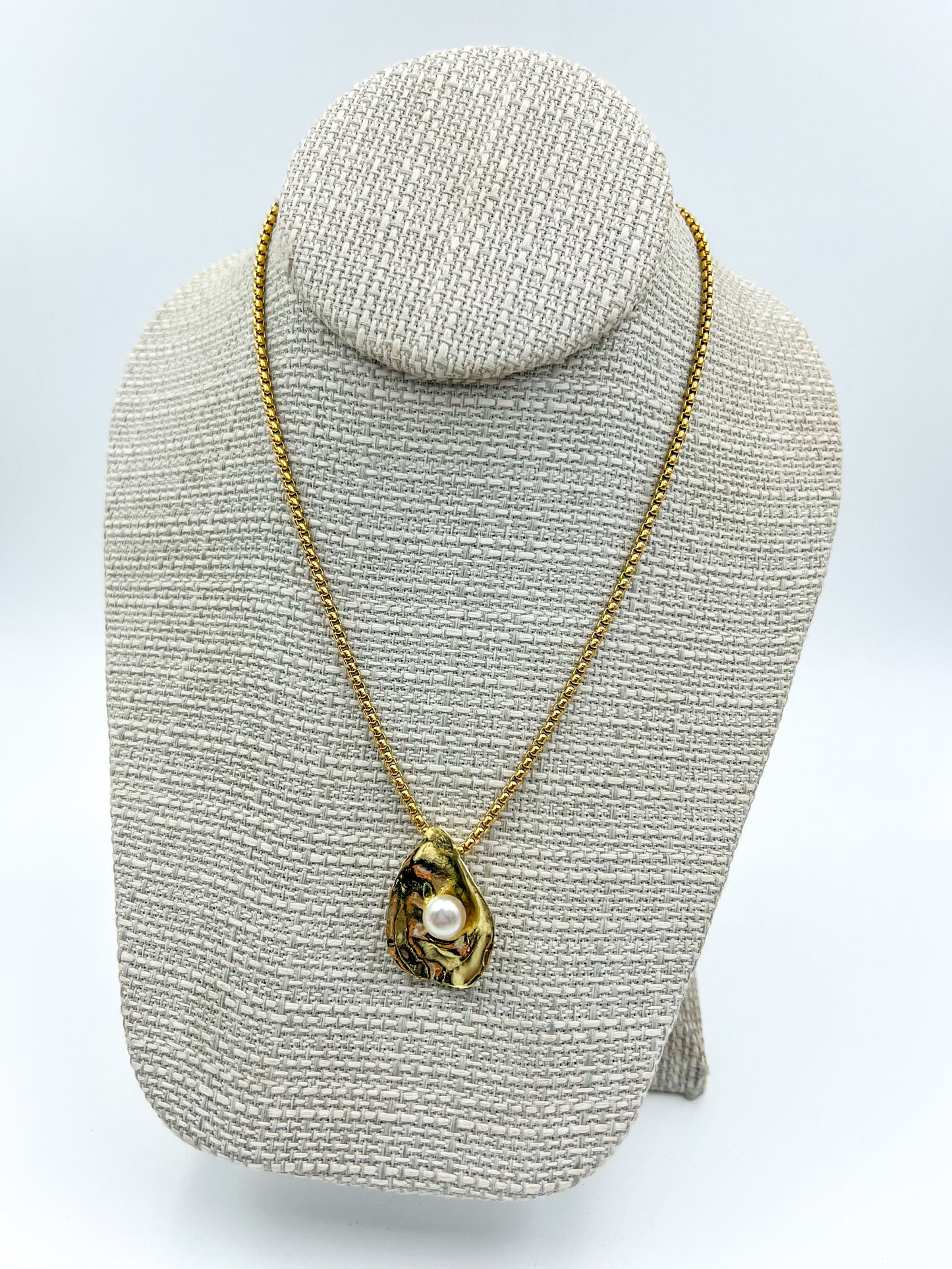 Gold necklace with a pendant on a gray textured stand against a white background