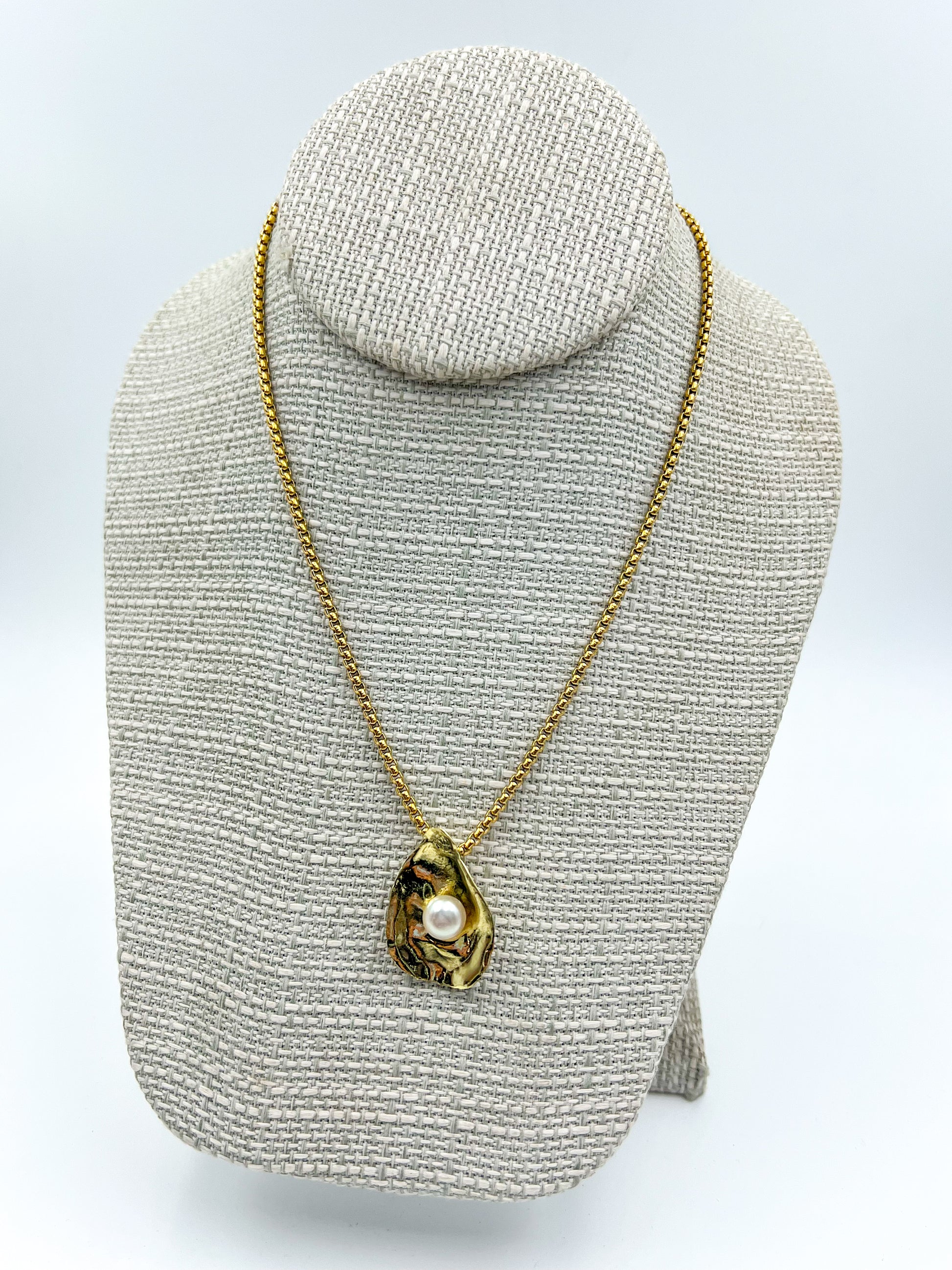 Gold necklace with a pendant on a gray textured stand against a white background