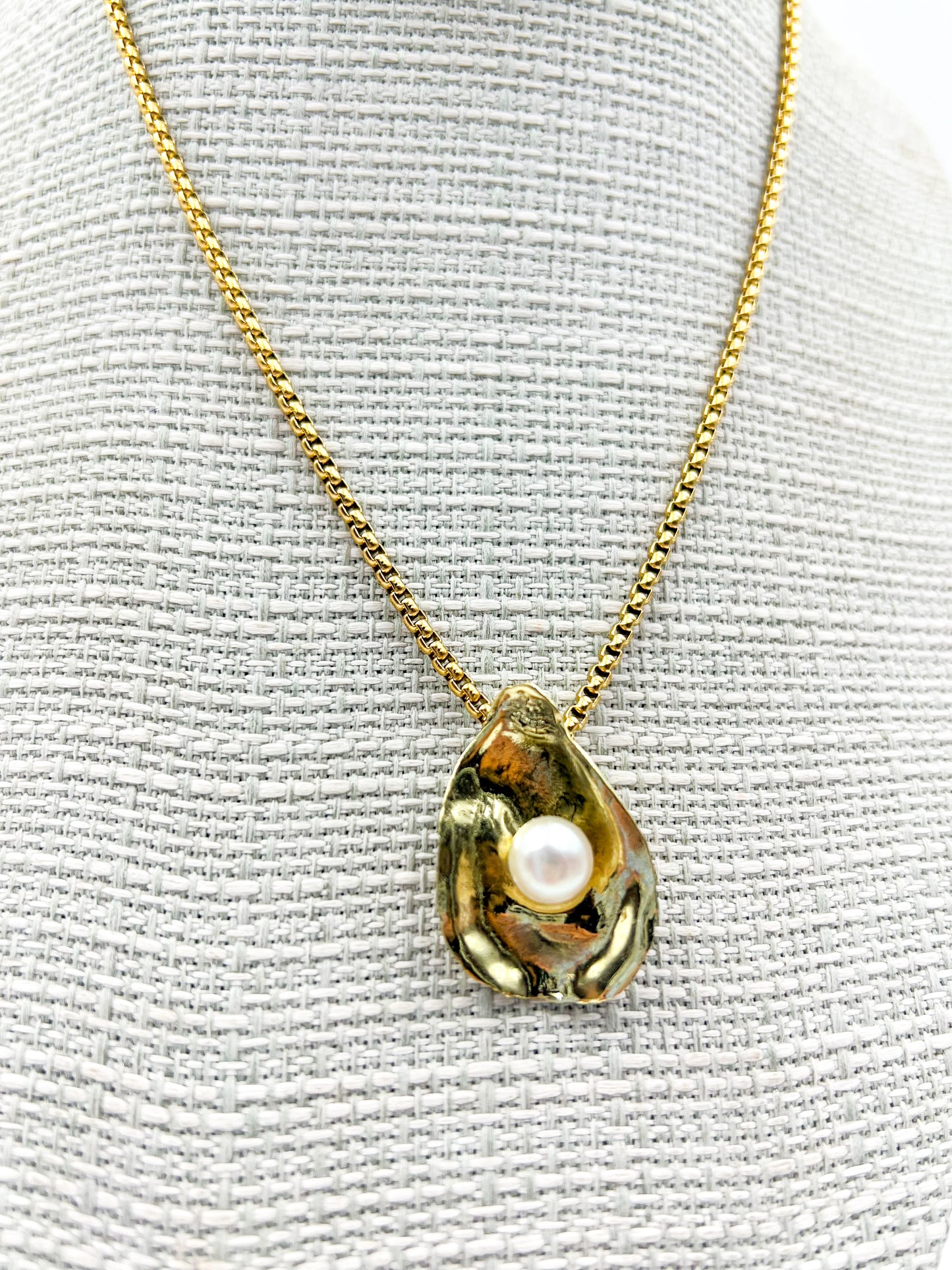Gold necklace with a oyster-shaped pendant featuring a pearl on a textured white background
