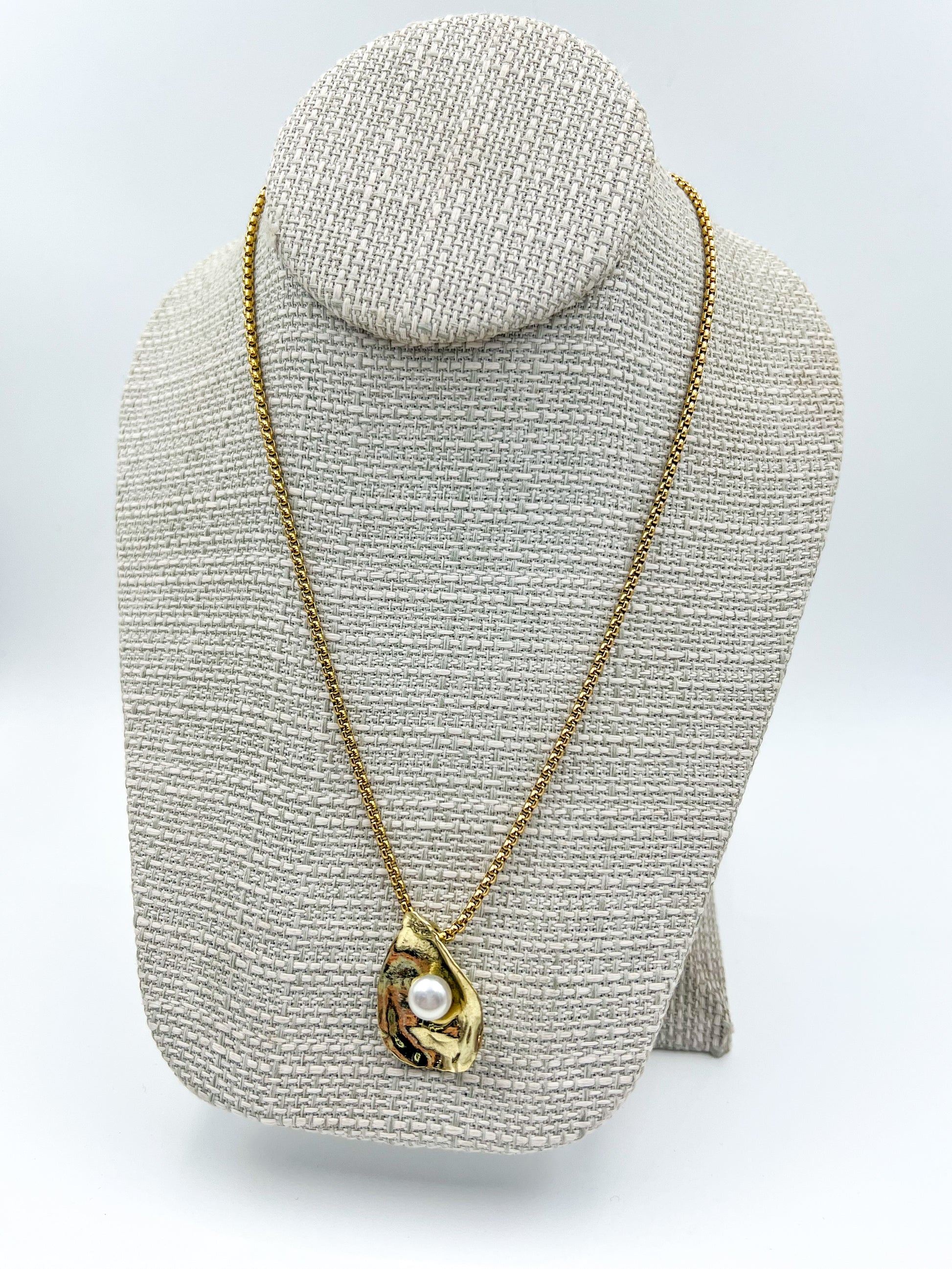 Gold necklace with a pendant on a textured gray stand against a white background