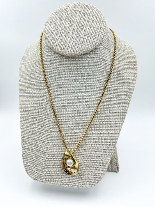 Gold necklace with a pendant on a textured gray stand against a white background