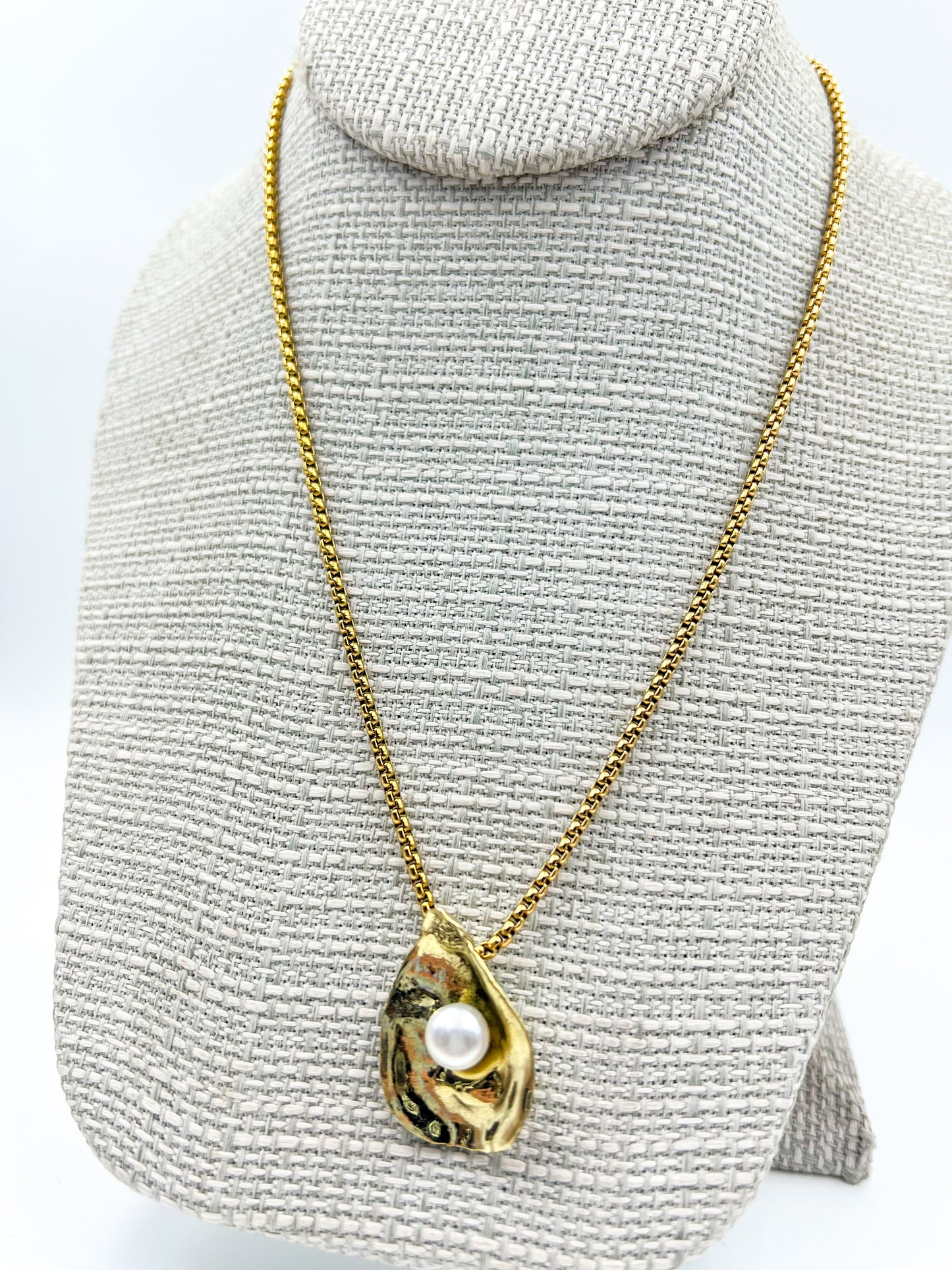 Gold necklace with a pendant on a gray textured stand