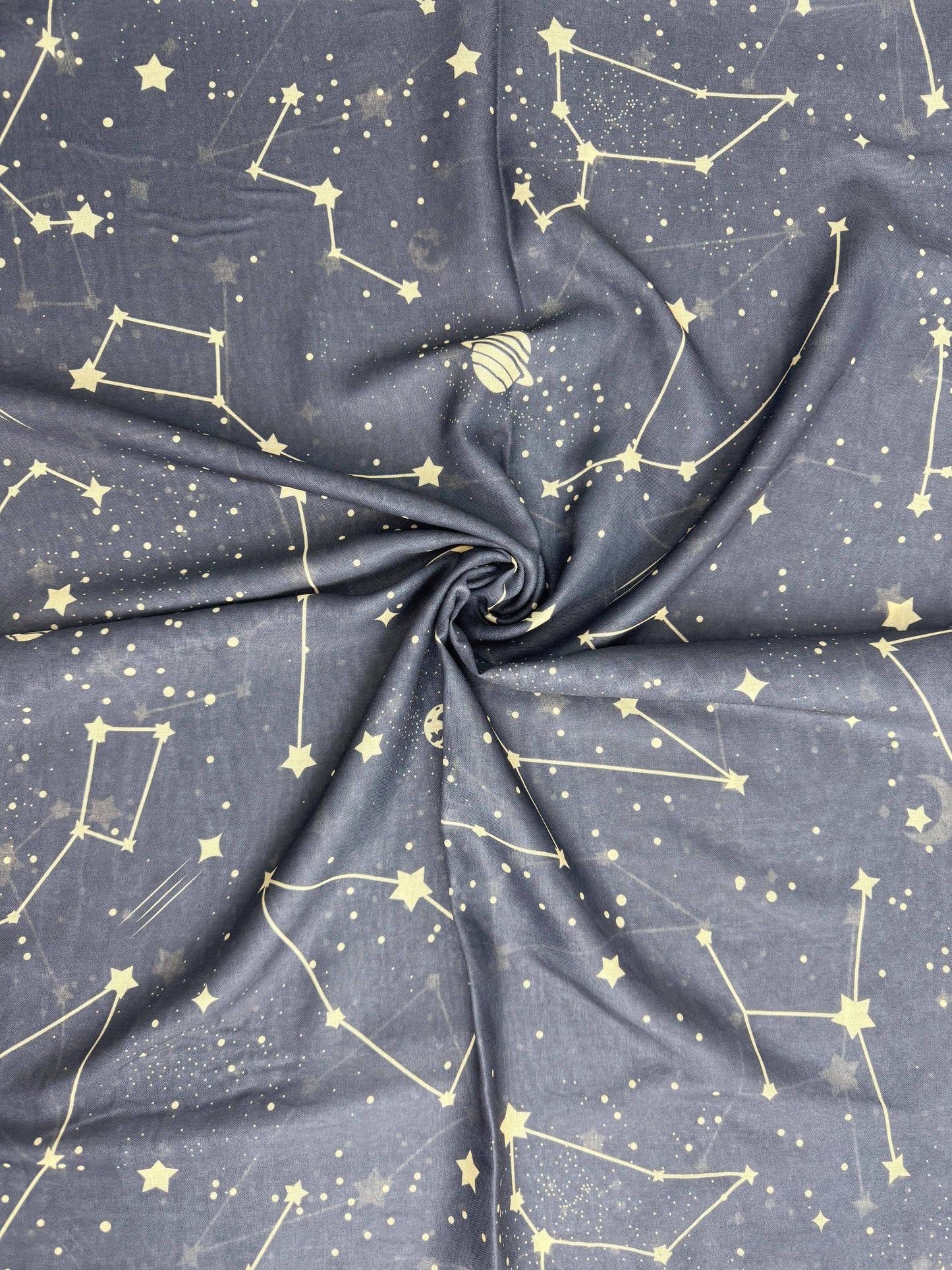 A close-up of draped fabric with a dark gray to navy base printed with a light yellow celestial pattern of stars, constellations, and small dots.