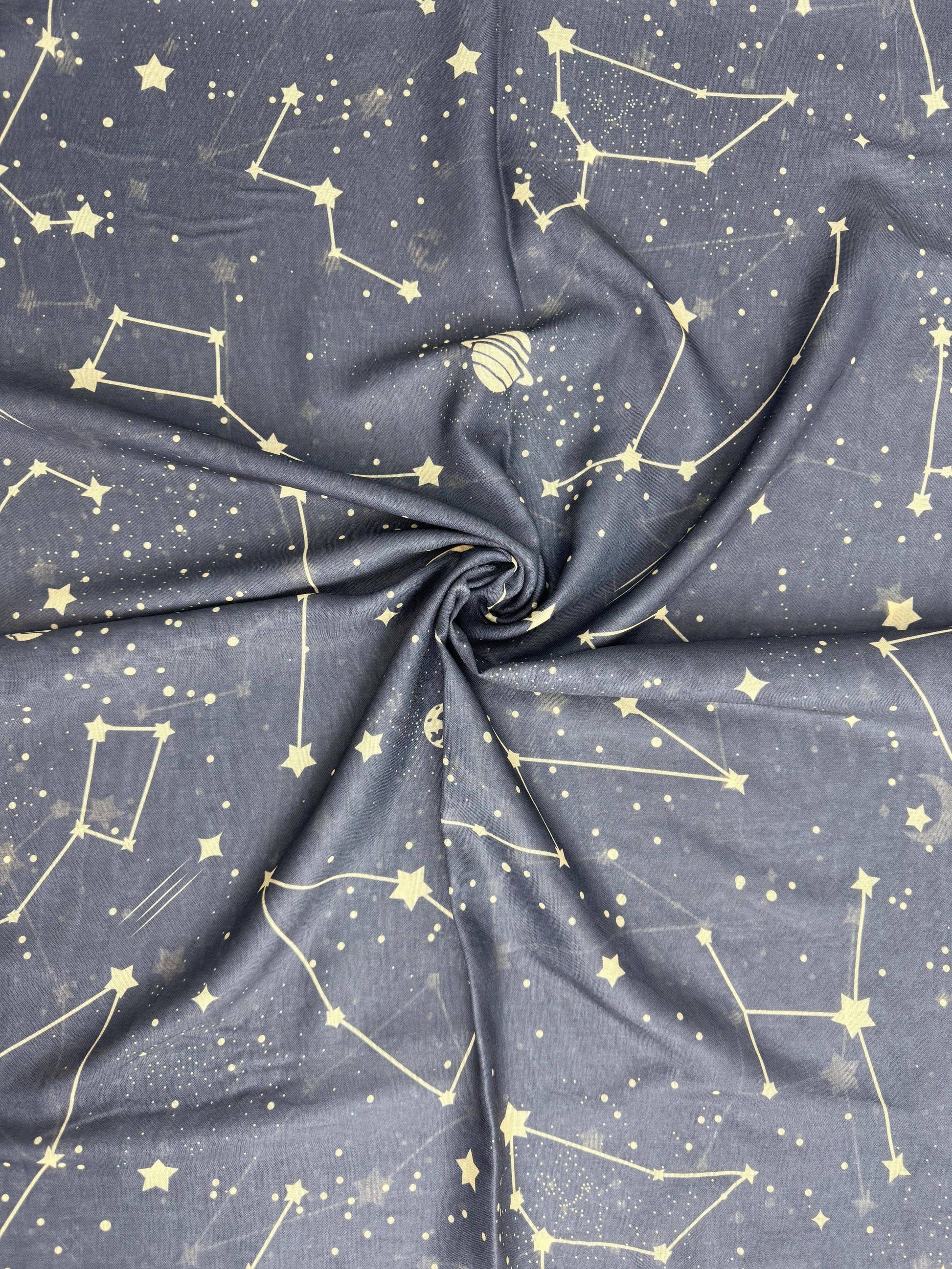 A close-up of draped fabric with a dark gray to navy base printed with a light yellow celestial pattern of stars, constellations, and small dots.