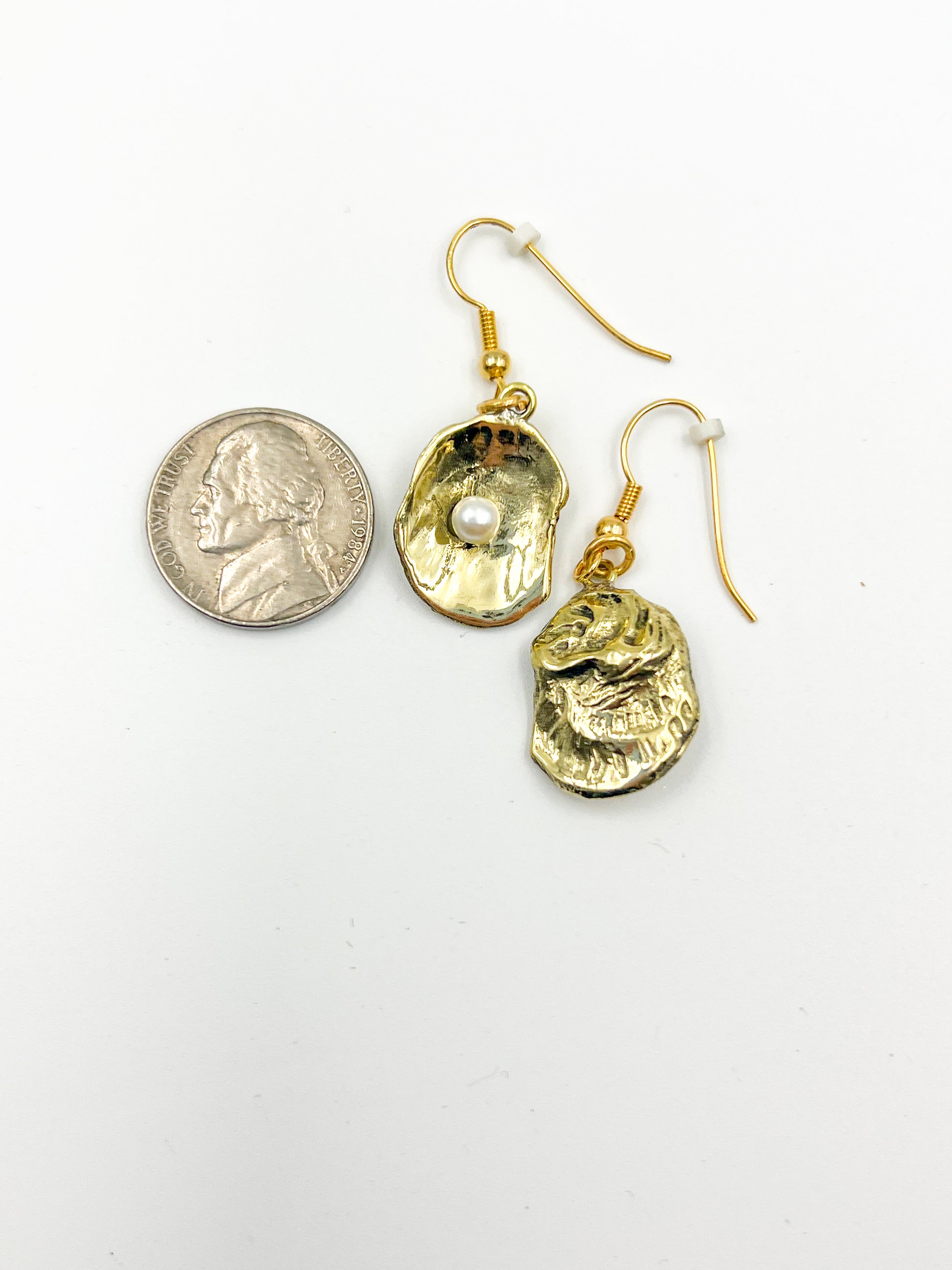 Gold earrings next to a nickle on a white background