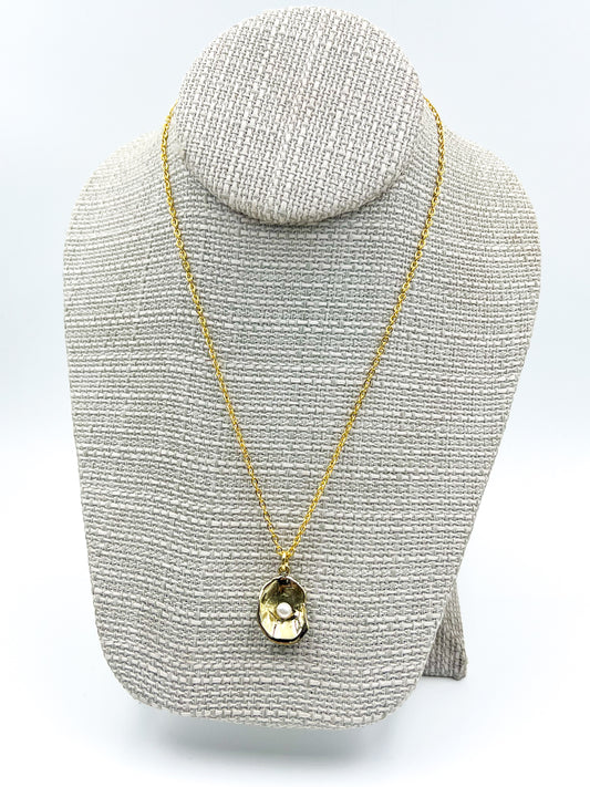 Gold necklace with a pendant on a gray textured stand against a white background