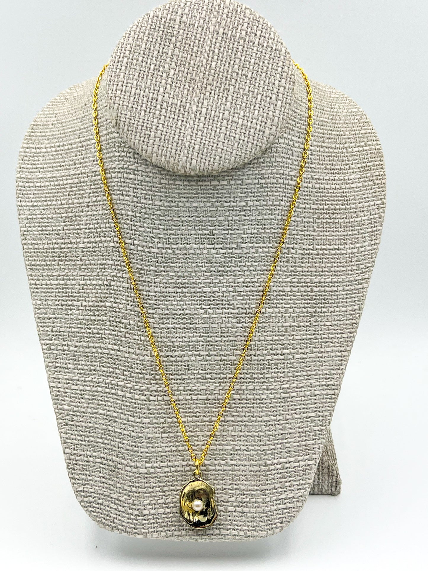 Gold necklace with a pendant on a gray textured stand against a white background