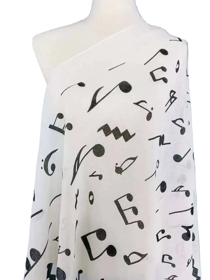 A white one-shoulder wrap or scarf draped on a mannequin, featuring an all-over black musical note print, set against a textured light blue background.
